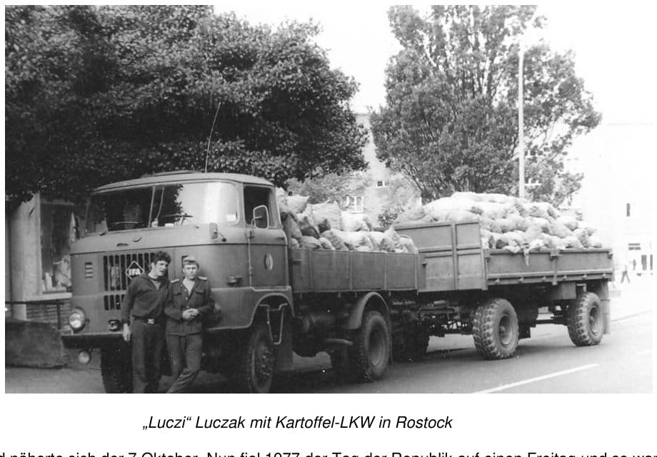 Ein IFA-Lastwagen mit Anhänger, beide voll mit Kartoffelsäcken beladen, steht in einer Straße; davor stehen zwei junge Männer in Arbeitskleidung